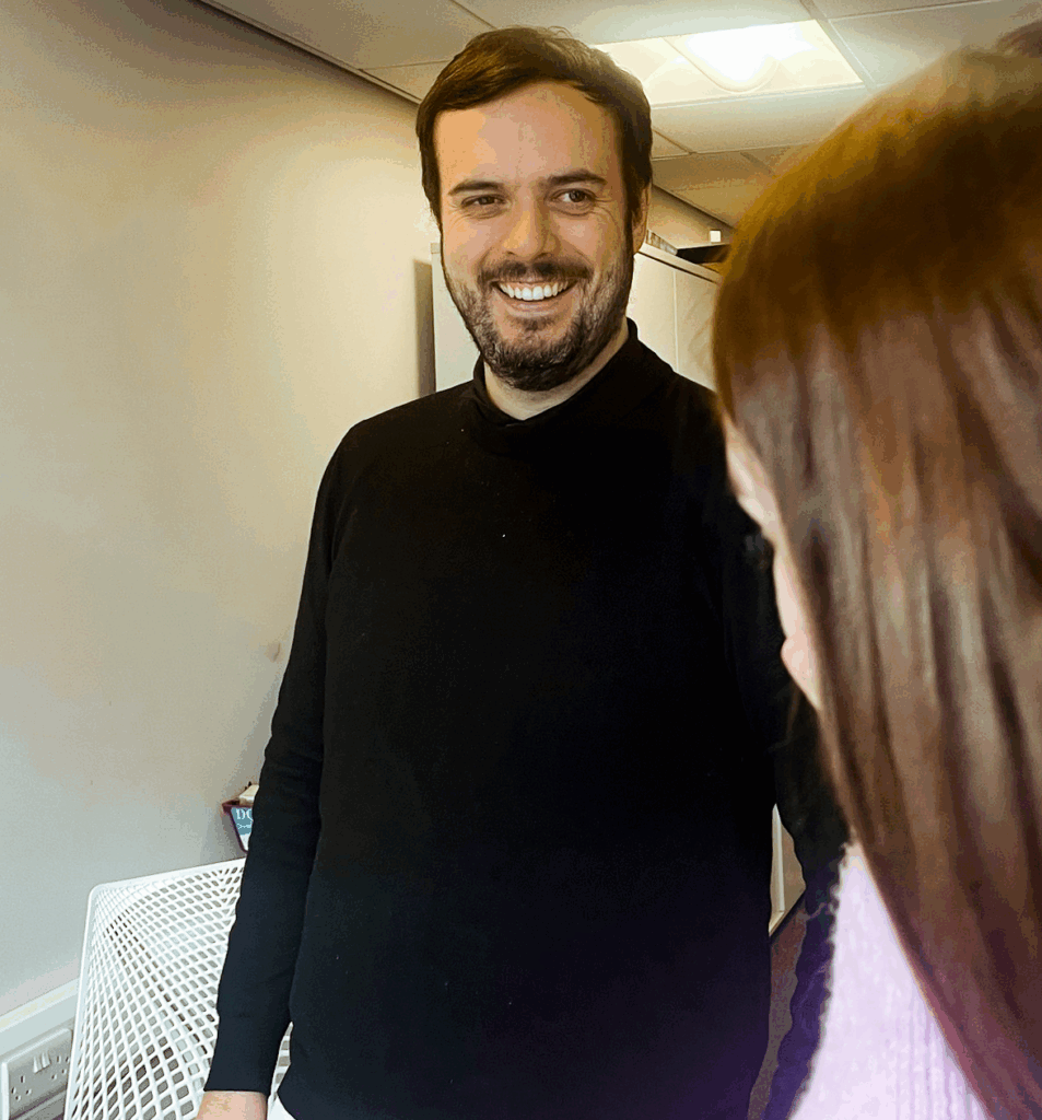 Man in a black turtleneck talking to colleague